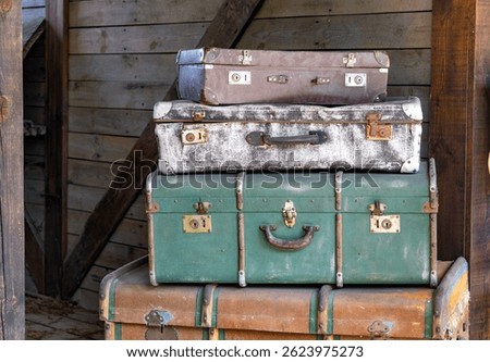 stack of old, weathered suitcases and trunks arranged in a rustic wooden setting. Each piece shows signs of age and use, giving the scene a strong vintage and nostalgic feel. Perfect for themes relate