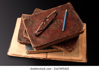 Stack Of Old Worn Jewish Books In Leather Binding On Open Torah Pages On Dark Background. Closeup. Selective Focus