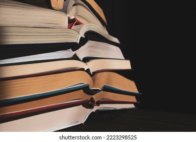 a stack of open books in the dark. The open books are stacked on top of each other. Books in a dark room in a vintage style. lots of books on a dark background. - Shutterstock ID 2223298525