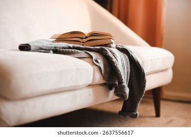 Stack of open paper books on knitted clothes on couch in living room at home. Cozy and hygge atmosphere. Coziness.