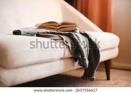 Stack of open paper books on knitted clothes on couch in living room at home. Cozy and hygge atmosphere. Coziness.