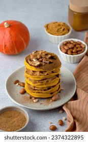 A stack of orange pumpkin pancakes, sprinkled with nuts, peanuts, cinnamon, peanut butter, pumpkin. An example of breakfast serving.