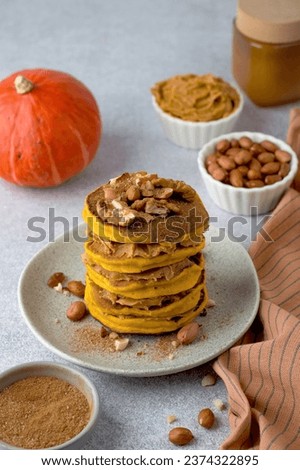 A stack of orange pumpkin pancakes, sprinkled with nuts, peanuts, cinnamon, peanut butter, pumpkin. An example of breakfast serving.