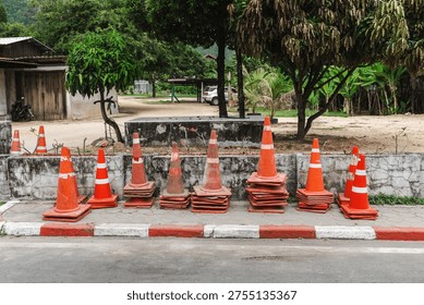 Stack of orange traffic cones on roadside near village street on Koh Samui Thailand.