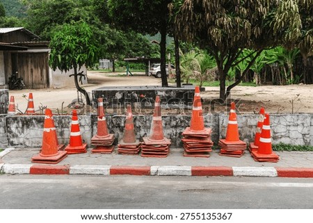 Stack of orange traffic cones on roadside near village street on Koh Samui Thailand.
