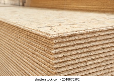 The stack of OSB sheets are stacked in a hardware store on a pallet. plywood with fragments of compressed sawdust, prepared for construction. Selective focus - Shutterstock ID 2018878592