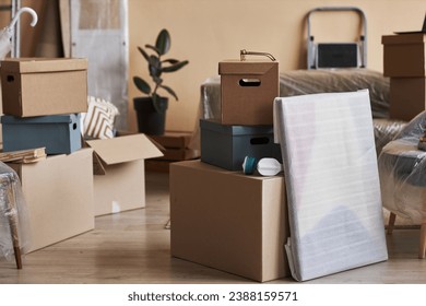 Stack of packed cardboard boxes and wrapped painting standing on the floor in the center of spacious living room of new apartment