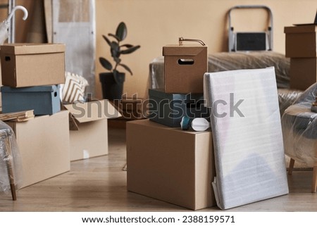 Stack of packed cardboard boxes and wrapped painting standing on the floor in the center of spacious living room of new apartment