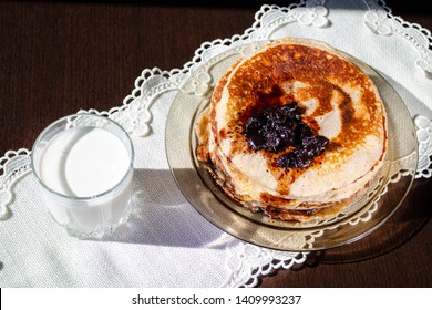 A stack of pancakes with cherry jam and a glass of milk on a linen napkin