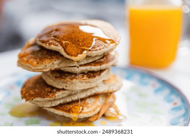 A stack of pancakes with dripping maple syrup and a glass of fresh orange juice