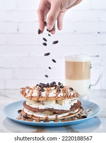 stack of pancakes with a hand adding chocolate beans and a latte in the background