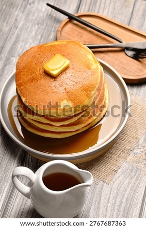 Stack of pancakes with melted butter and a white jar of honey on the side