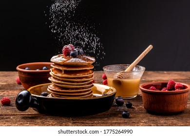 Stack of pancakes with sugar powder splashes on dark background table. homemade classic american pancakes with fresh berry and honey. Copy space for your text.