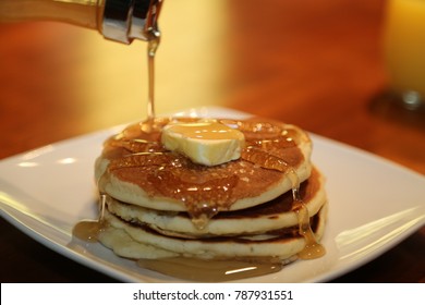 Stack of pancakes with syrup pouring over them.