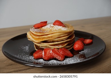 Stack of pancakes topped with maple syrup, strawberry pieces, and powdered sugar.