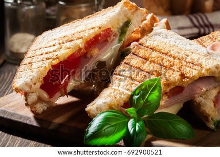 Stack of panini with ham, cheese and lettuce sandwich on a cutting board