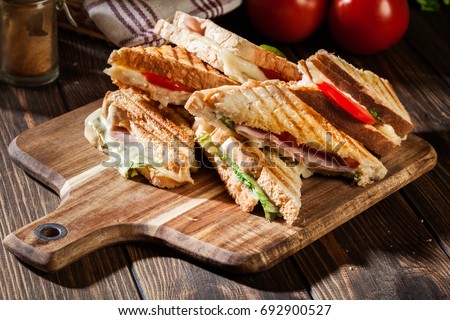 Stack of panini with ham, cheese and lettuce sandwich on a cutting board