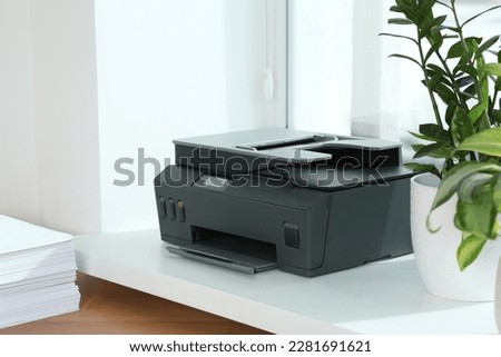 Stack of paper on wooden table near window sill with modern printer in office