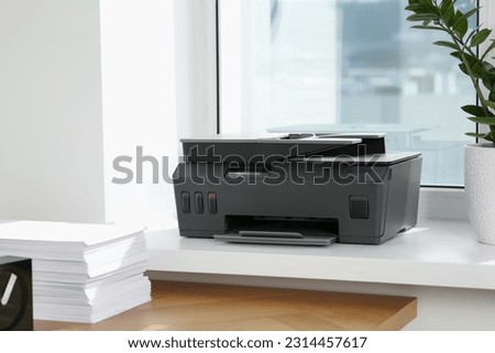 Stack of paper on wooden table near window sill with modern printer in office