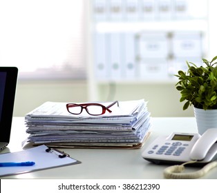 a stack of papers on the desk with a computer