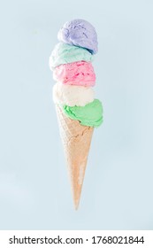 Stack of pastel colorful ice cream scoops in waffle cone, isolated on light blue background. Woman hand holds big ice cream cone with different flavor scoops