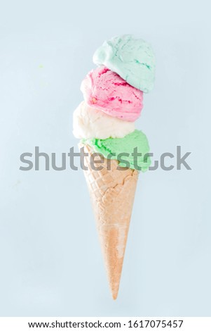 Stack of pastel colorful ice cream scoops in waffle cone, isolated on light blue background. Woman hand holds big ice cream cone with different flavor scoops