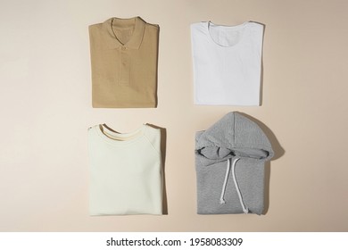 Stack of pastel perfectly folded cotton polo, t shirt, hoodie and sweat shirt isolated over pale beige background. Minimalism concept. Template. Copy space. Horizontal shot