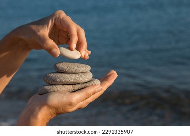 Stack pebbles rising in a pyramid shape in woman's hand, sea background. Personal growth, success, motivation, meditation and Zen concepts. Horizontal close-up.