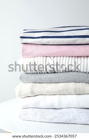 Stack of perfectly folded clothing items. Pile of different pastel color shirts, sweaters and other garments on table