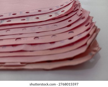 A stack of pink continuous form paper with perforations on the sides, photographed close-up with focus on the texture and edge details. Suitable for administrative concepts, legacy data, record-keeping, and classic documentation systems.