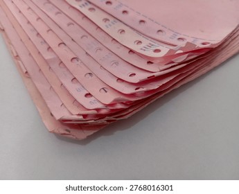 A stack of pink continuous form paper with perforations on the sides, photographed close-up with focus on the texture and edge details. Suitable for administrative concepts, legacy data, record-keeping, and classic documentation systems.