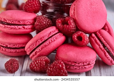 A stack of pink macarons with raspberries on a wooden table, showcasing a delicious dessert made with natural ingredients and baked goods