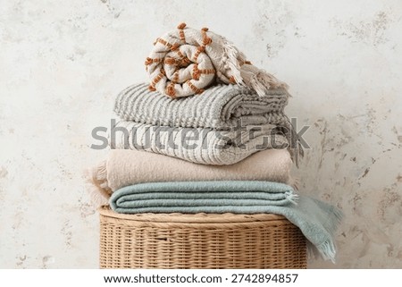 Stack of plaids on basket near light grunge wall