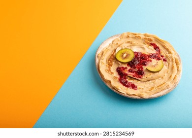 Stack of Plain Fried pancakes with jam and kiwi on blue and orange pastel paper background. side view, copy space