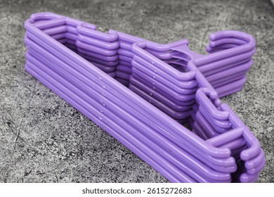 Stack of Plastic Clothes Hangers with Trouser Bar and Shoulder Notches Hangers for Clothes Good Quality Plastic Hangers with purple color.