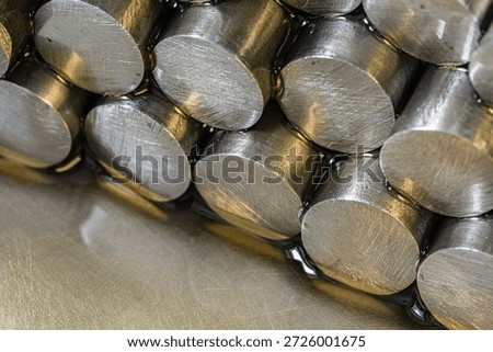 Stack of precious metal rods lying on an oil-covered metal surface with visible circular cross sections in industrial lighting. Concept of metallurgy, manufacturing, raw materials, heavy industry and metal processing.
