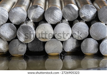 Stack of precious metal rods lying on an oil-covered metal surface with visible circular cross sections in industrial lighting. Concept of metallurgy, manufacturing, raw materials, heavy industry and metal processing.