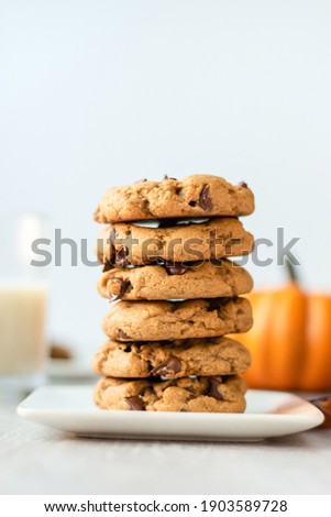 stack of pumpkin chocolate chip cookies with a glass of milk and pumpkin decoration