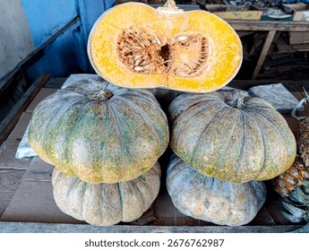 Stack of pumpkins, one sliced open to reveal orange flesh and seeds.  Market stall setting.