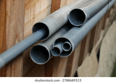 Stack of PVC plastic pipes in various sizes stored next to a wooden fence.
