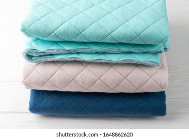 A Stack Of Quilted Knit Fabric For Sewing Mint, Blue And Blush Blankets On A White Wooden Table.