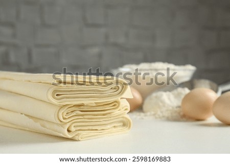 Stack of raw puff pastry dough on white table, closeup. Space for text