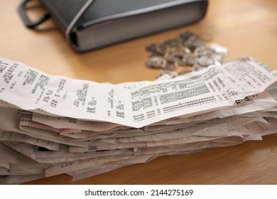 A Stack Of Receipts In The Foreground With Coins And Accordion Folder Organizer In Background