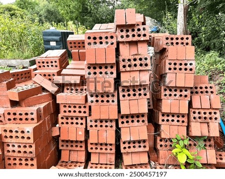 A stack of red bricks covered in cobwebs in a garden.  the bricks alternate with face and side on, some with airholes showing in an abstract pattern