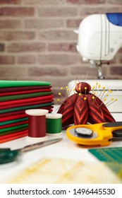 Stack of red and green fabrics, sewing and quilting accessories and sewing machine on brick wall background