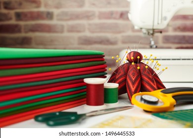 Stack of red and green fabrics, sewing and quilting accessories and sewing machine on brick wall background