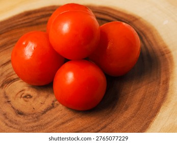 A stack of red juicy tomatoes sits on a wooden table. The tomatoes are arranged in a neat row, and they appear to be fresh and ripe