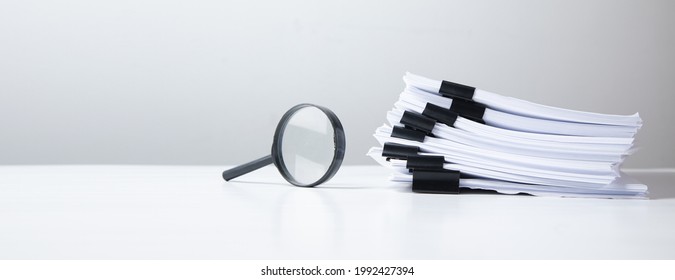 Stack of report paper documents with magnifying glass. Concept of business and search.