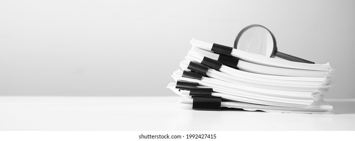 Stack of report paper documents with magnifying glass. Concept of business and search.