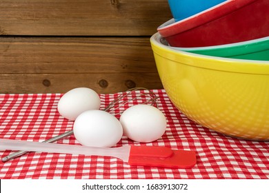 stack of retro mixing bowls on checkered tablecloth with white eggs and kitchen utensils